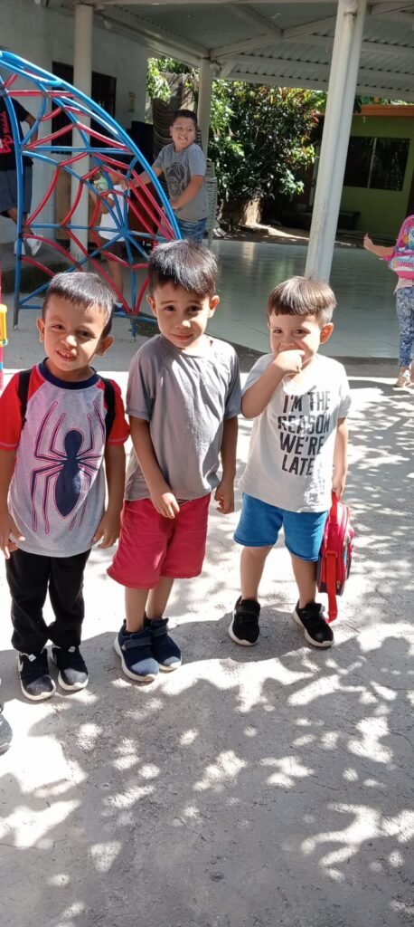 Tres niños sonriendo en el patio de la iglesia bautista, listos para participar en actividades al aire libre.