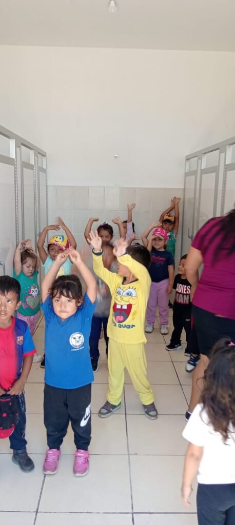 Un grupo de niños en una sala de actividades, levantando las manos y disfrutando de un momento divertido en la iglesia bautista.